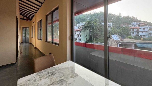 Un couloir d’hôtel avec une table et des chaises surmontées d’un plateau en marbre, de grandes fenêtres et une vue sur les bâtiments environnants.