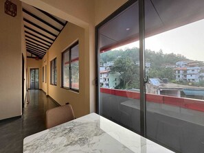 A hotel corridor with a marble-topped table and chairs, large windows, and a view of the surrounding buildings. - UDF City Hotel Kandy (Kandy)