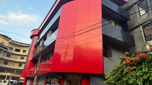 Un hôtel à la façade rouge et grise, avec une entrée bien visible et une enseigne indiquant « CHAMBRES D’HÔTEL ».