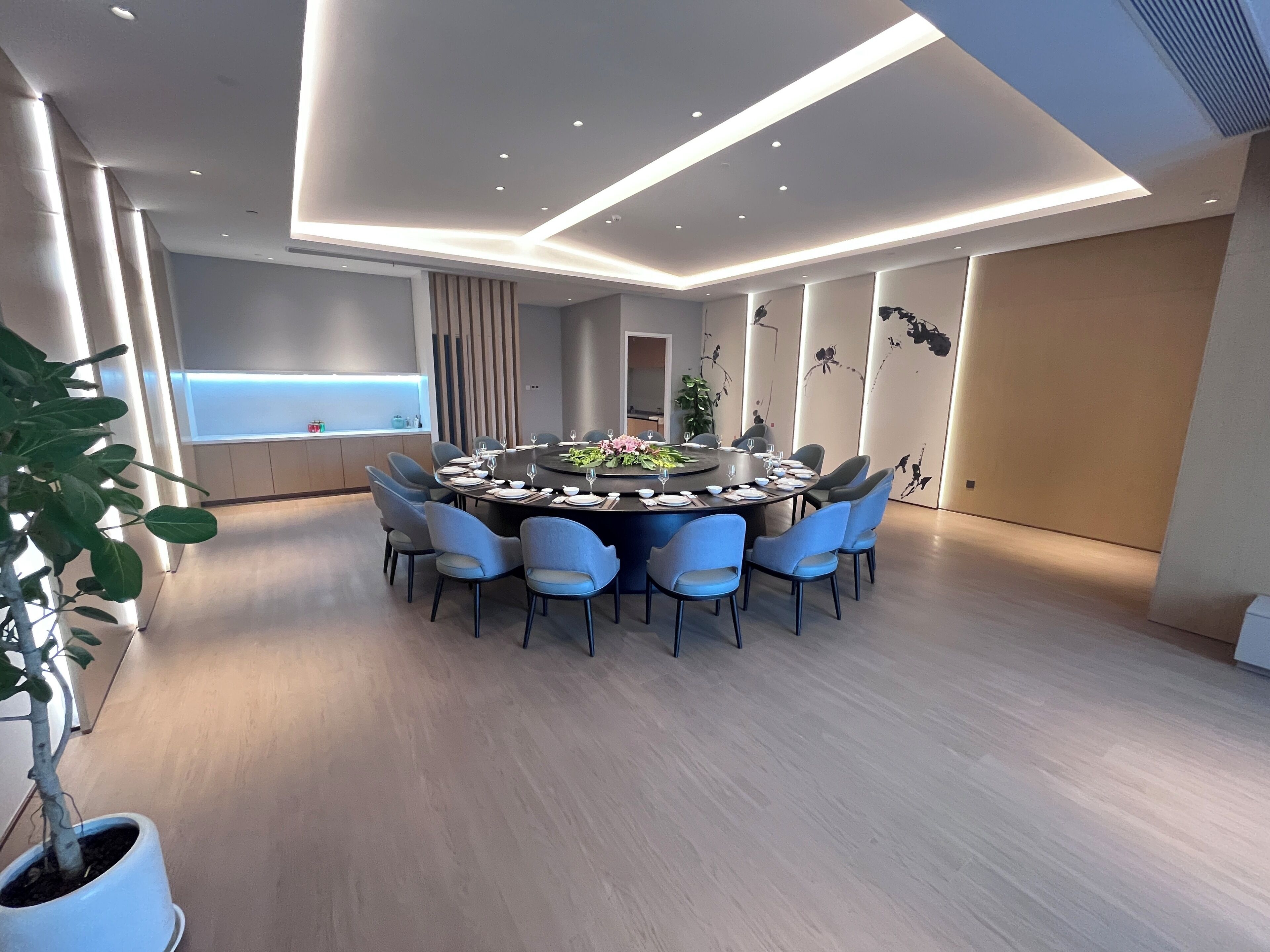 A modern dining area with a round table, blue chairs, and a potted plant.