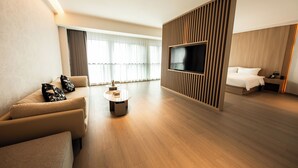 A modern hotel room with a sofa, a coffee table, a TV mounted on a wooden panel, a bed, and a nightstand. - LES AIRS (Wenzhou)