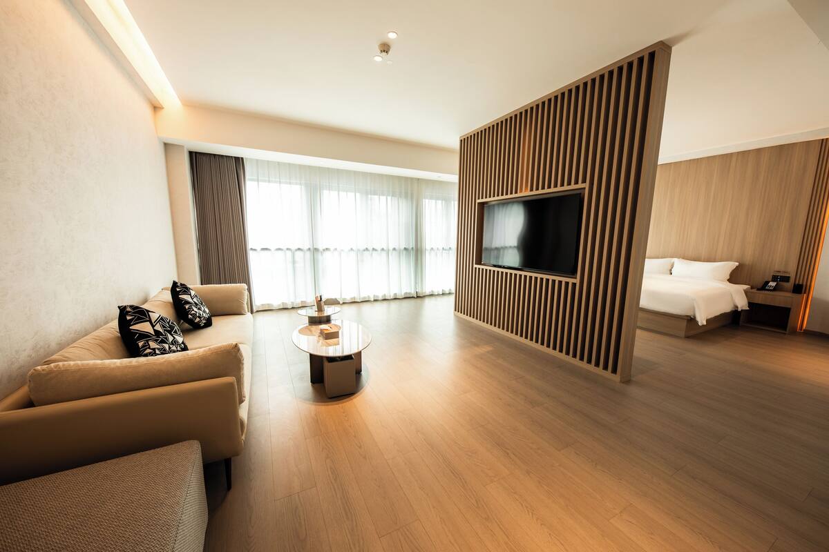 Ein modernes Hotelzimmer mit Sofa, Couchtisch, einem an einer Holzplatte montierten Fernseher, Bett und Nachttisch.