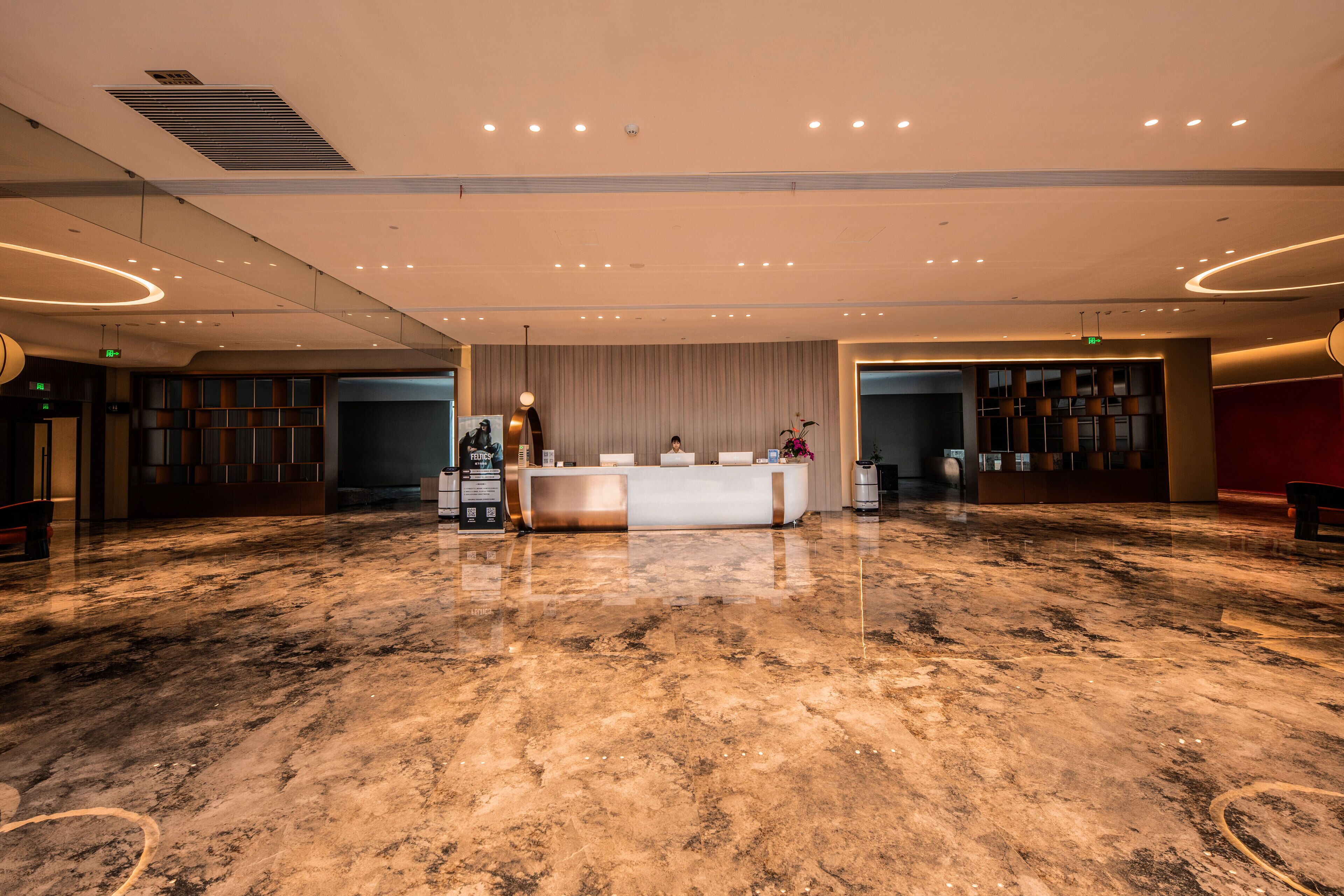 A spacious lobby with a reception desk, marble flooring, and modern lighting fixtures.
