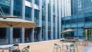 An outdoor seating area with tables and chairs, a wooden deck, and a modern building with large windows in the background. - LES AIRS (Wenzhou)