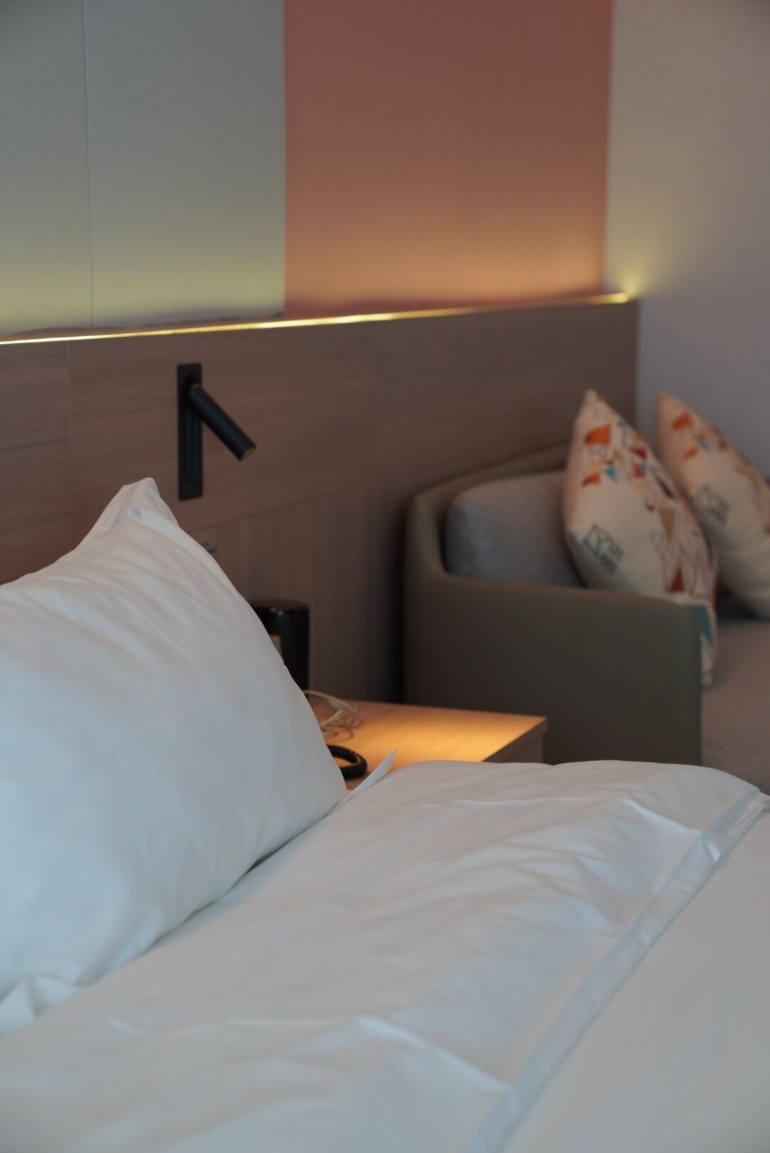A neatly made bed with white linens, a bedside lamp, and a wall-mounted light fixture.