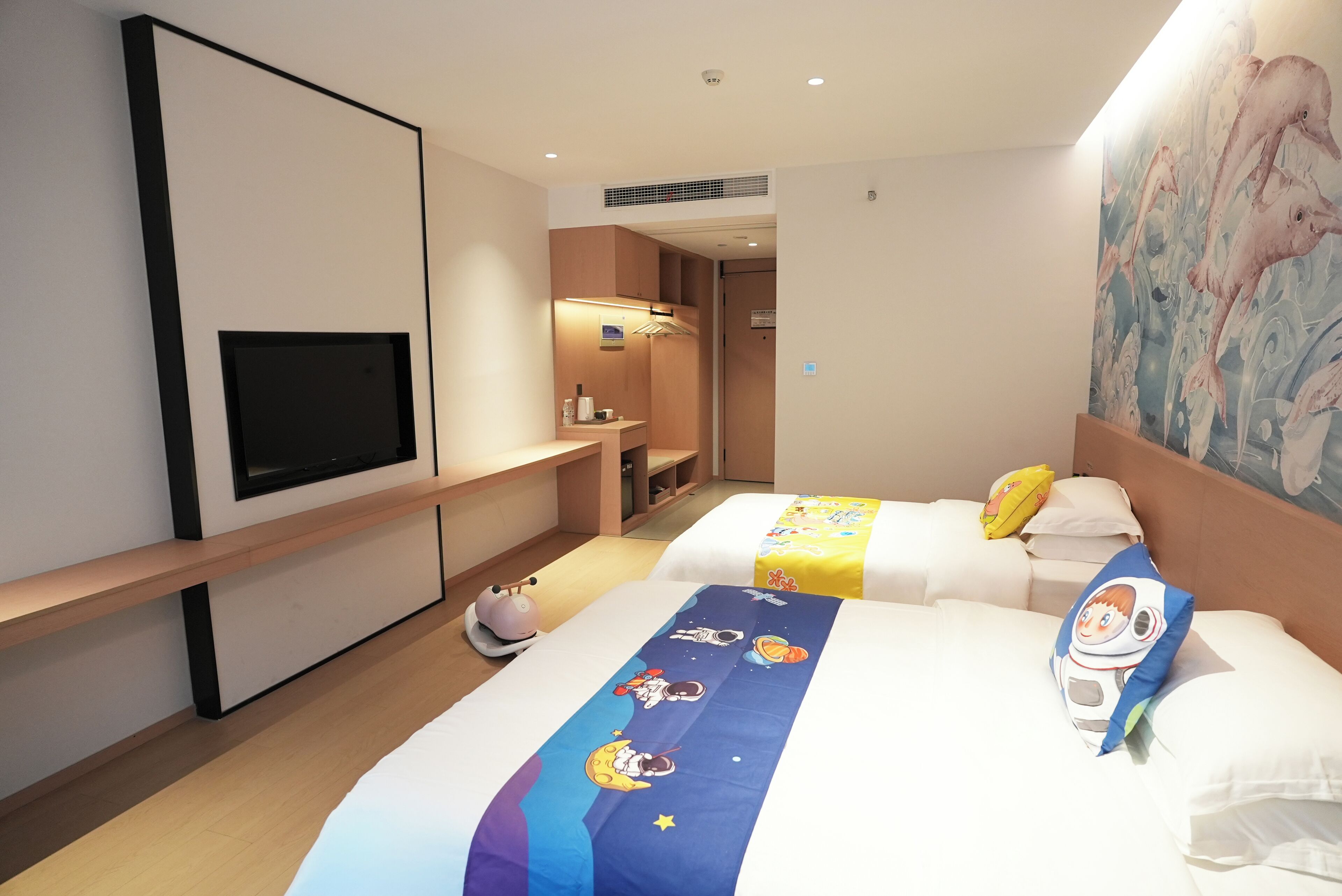 Ein Hotelzimmer mit zwei Betten, einem Fernseher, einem Bild und einem sichtbaren Badezimmer im Hintergrund.