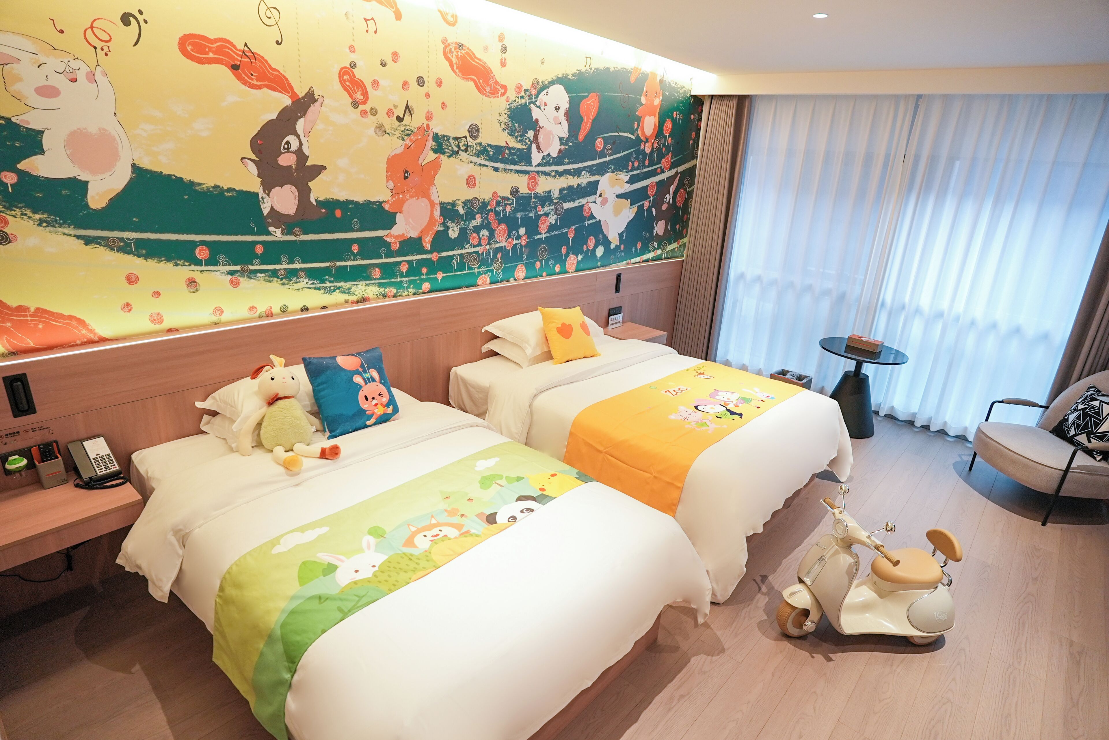 A hotel room with two beds, a mural on the wall, a small table, and a scooter.