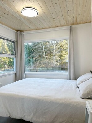 A bedroom with a large bed, a window with curtains, and a ceiling light.