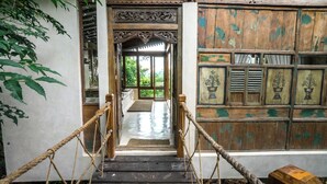 A wooden staircase with rope railings leading to a room with traditional wooden doors and a view of greenery outside.