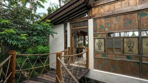 A rustic wooden building with a rope barrier, a wooden staircase, and a window with a floral design.