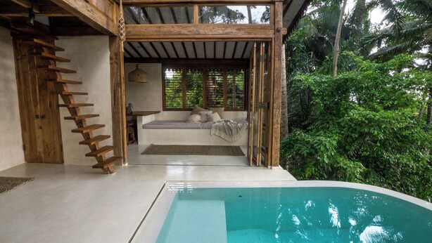 A wooden staircase leading to a covered seating area with a pool in the foreground.