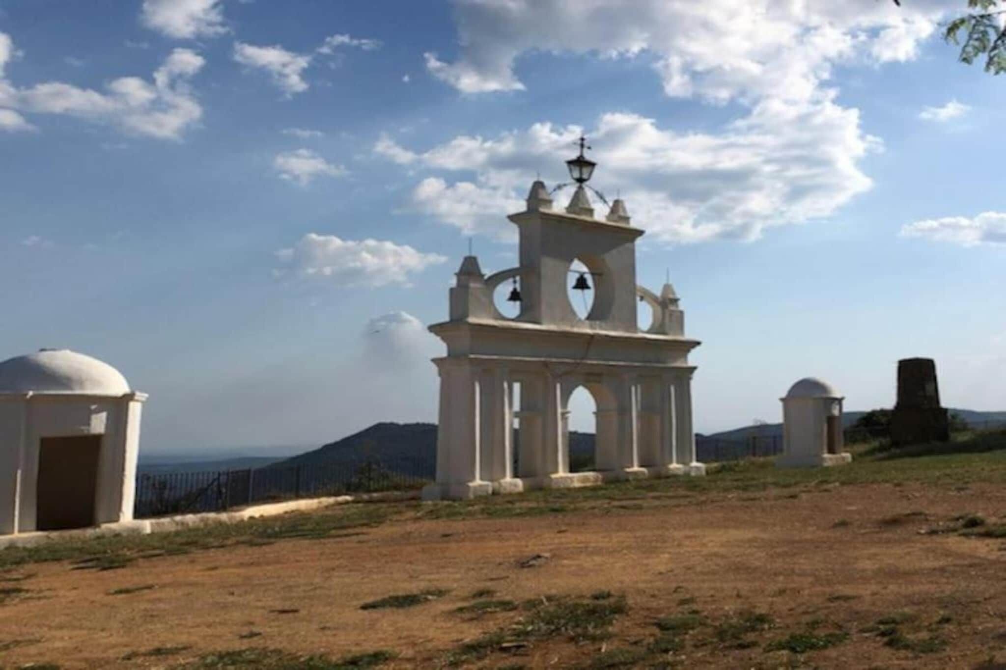 Una torre de campana blanca con cúpula y una campana, rodeada por una zona cercada bajo un cielo despejado.