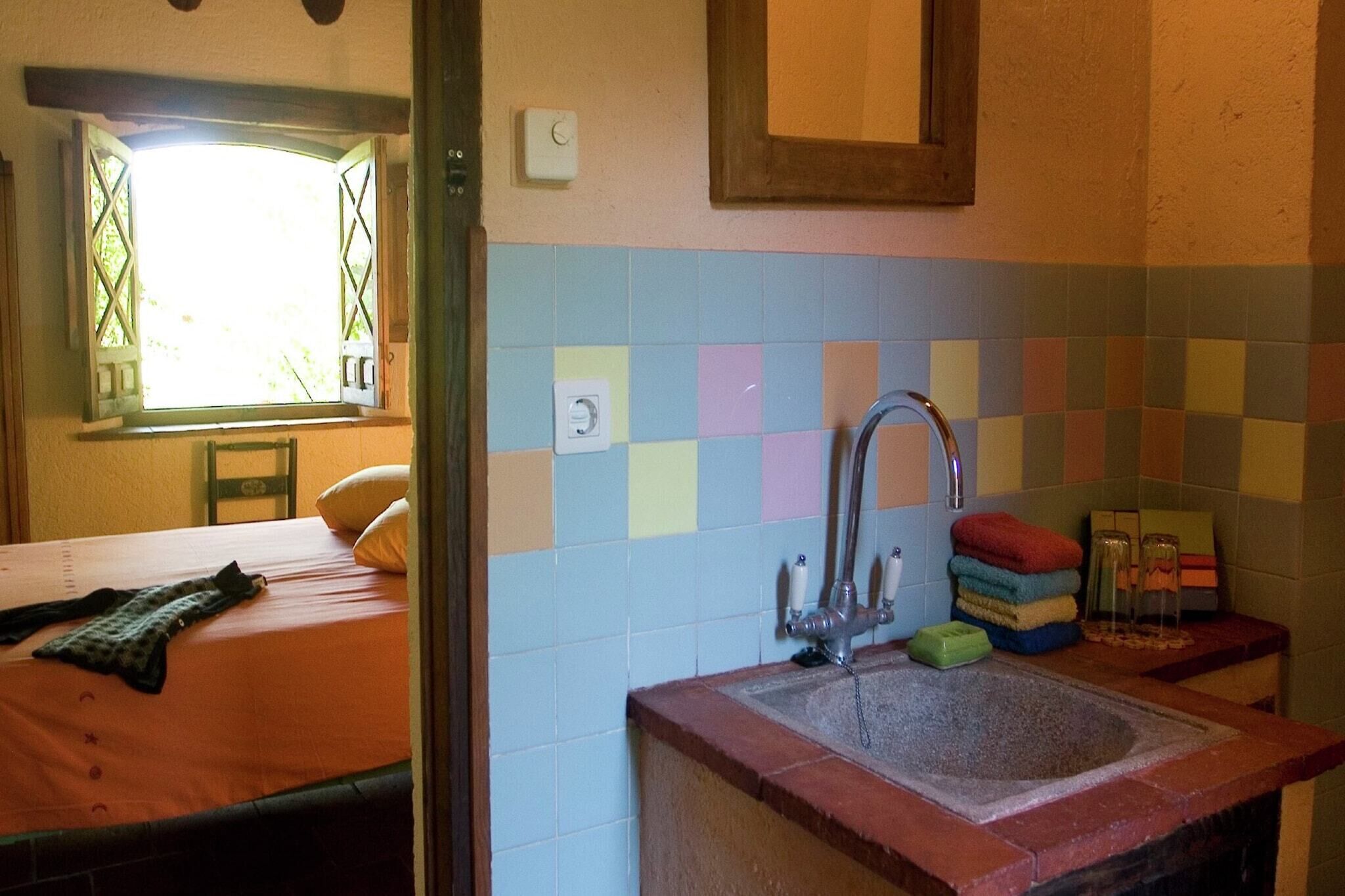 A room with a bed, a window with a view, a sink with a faucet, and a tiled backsplash.