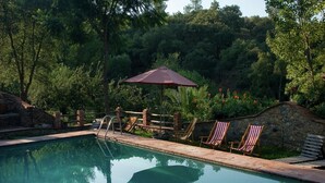 A swimming pool with a stone wall, wooden deck, and lounge chairs. - El Águila, Stone Cottage (Alájar)