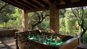 A foosball table under a wooden pergola with brick pillars, surrounded by lush greenery. - El Águila, Stone Cottage (Alájar)