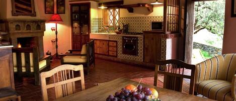 A cozy kitchen with wooden furniture, a dining table with fruit, and a fireplace.