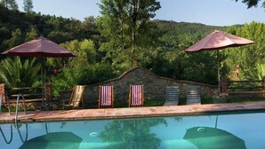 A swimming pool with stone walls, two umbrellas, and a stone building with striped awnings. - El Búho, Cottage in Alájar (Alájar)