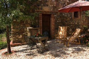 A stone building with a wooden table and chairs, an umbrella, and a potted plant. - El Búho, Cottage in Alájar (Alájar)