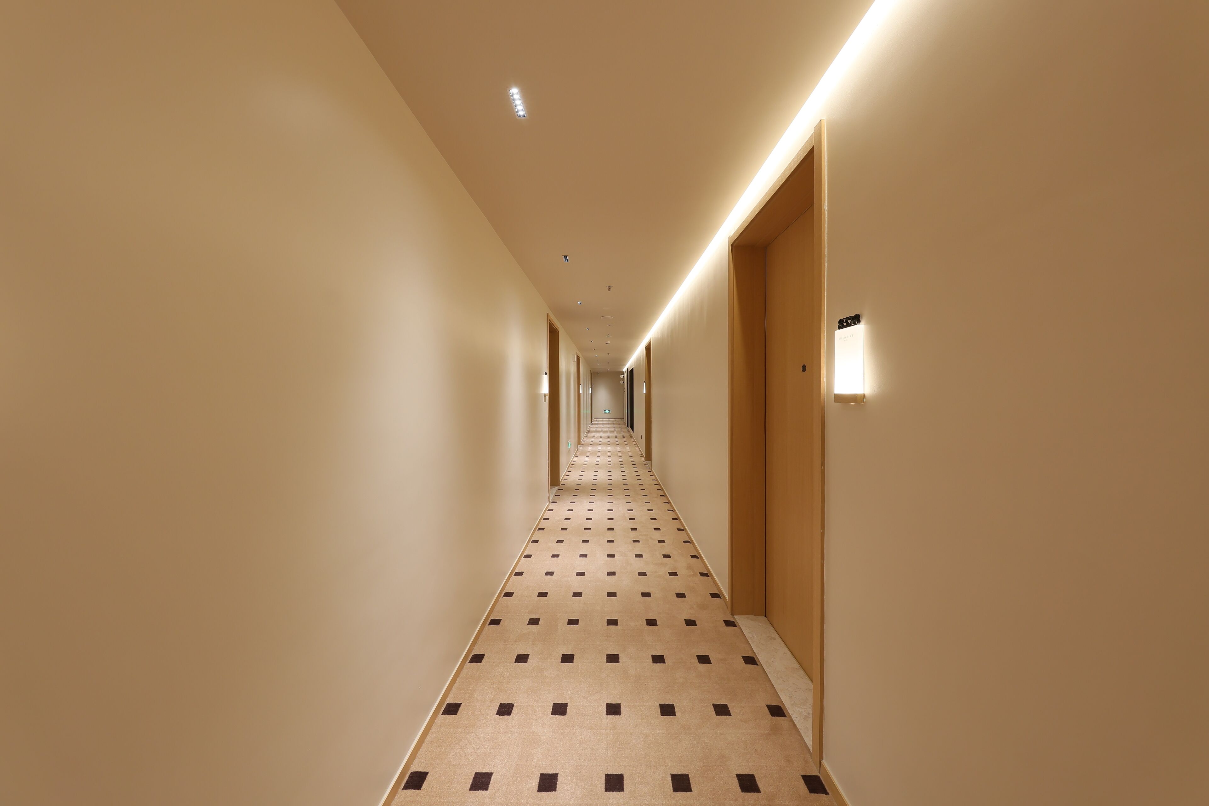A hotel hallway with a patterned carpet, wooden doors, and recessed lighting.
