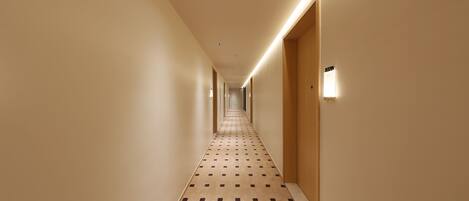 A hotel hallway with a patterned carpet, wooden doors, and recessed lighting.