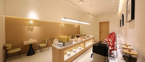 Un moderno vestíbulo de hotel con una recepción, zona de estar y un bufé con diferentes opciones de comida.