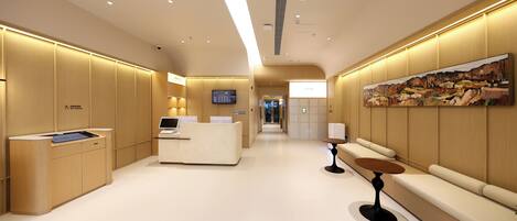 A modern hotel lobby with a reception desk, seating area, and a large painting on the wall.
