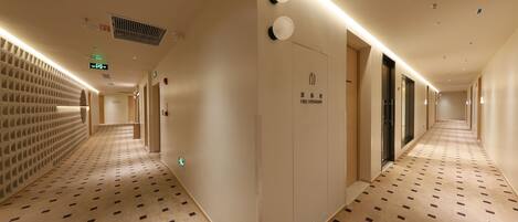 A hotel corridor with patterned carpet, recessed lighting, and a fire hydrant sign.