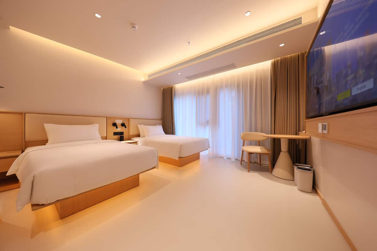 A modern hotel room with two beds, a desk, and a TV.