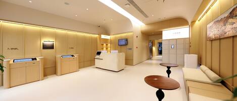 A modern hotel lobby with a reception desk, seating area, and a TV screen.