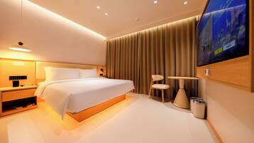 A modern hotel room with a large bed, bedside table, lamp, TV, and a small table with a chair.