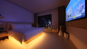 Habitación de hotel moderna con una cama grande, un escritorio y una televisión que muestra una vista urbana.