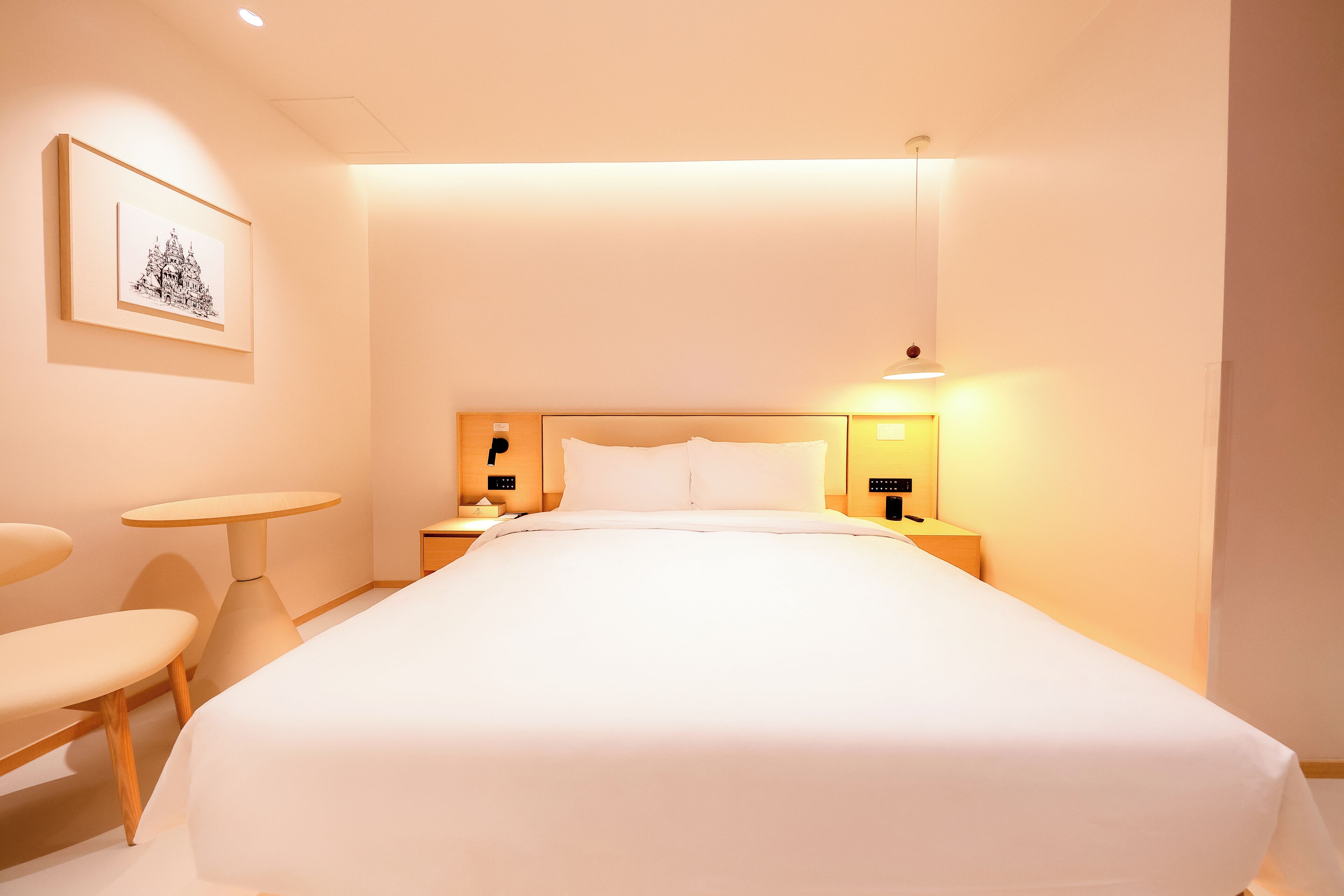 Une chambre d’hôtel avec un grand lit, des tables de chevet, une petite table ronde et un tableau encadré au mur.