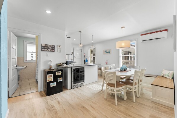 A modern kitchen with a dining area, a refrigerator, a sink, and a window overlooking the interior.