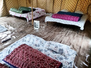Une chambre avec deux lits, l’un recouvert d’une couverture verte et l’autre d’une couverture rose et bleue. Il y a un radiateur sur le sol et une multiprise avec un chargeur de téléphone.