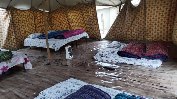 A tented accommodation with multiple beds, a fan, and a remote control on the floor. - Maha Kumbh Camp (Phulpur)