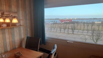 Ein Zimmer mit Holztisch, Stühlen und einem Fenster mit Blick auf ein weit entferntes Gebäude und Bäume.