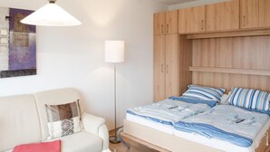 A bedroom with a bed, a nightstand, a floor lamp, and a wardrobe. - Holiday Home in Fehmarn near Beach (Fehmarn)