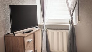 A room with a wooden cabinet, a television, a remote control, and a window with curtains.