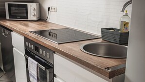 A modern kitchen with white cabinetry, a wooden countertop, a built-in oven, a microwave, and a stainless steel sink.