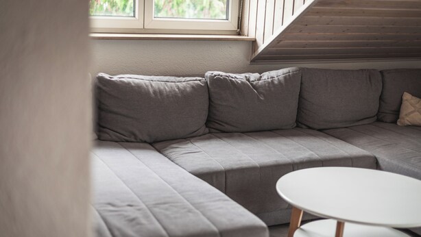 A grey sectional sofa with a white round table in a room with wooden beams on the ceiling.