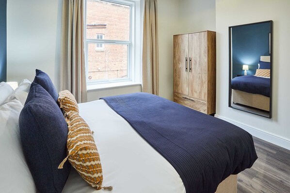 A neatly made bed with a blue and white duvet, two pillows, and a patterned throw. A wooden wardrobe is beside the bed, and a mirror hangs on the wall. - Host Stay Apartment 3 Upton House (Northampton)
