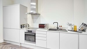 A modern kitchen with white cabinetry, a built-in oven, a microwave, and a stainless steel range hood. - Host Stay Apartment 1 Upton House (Northampton)