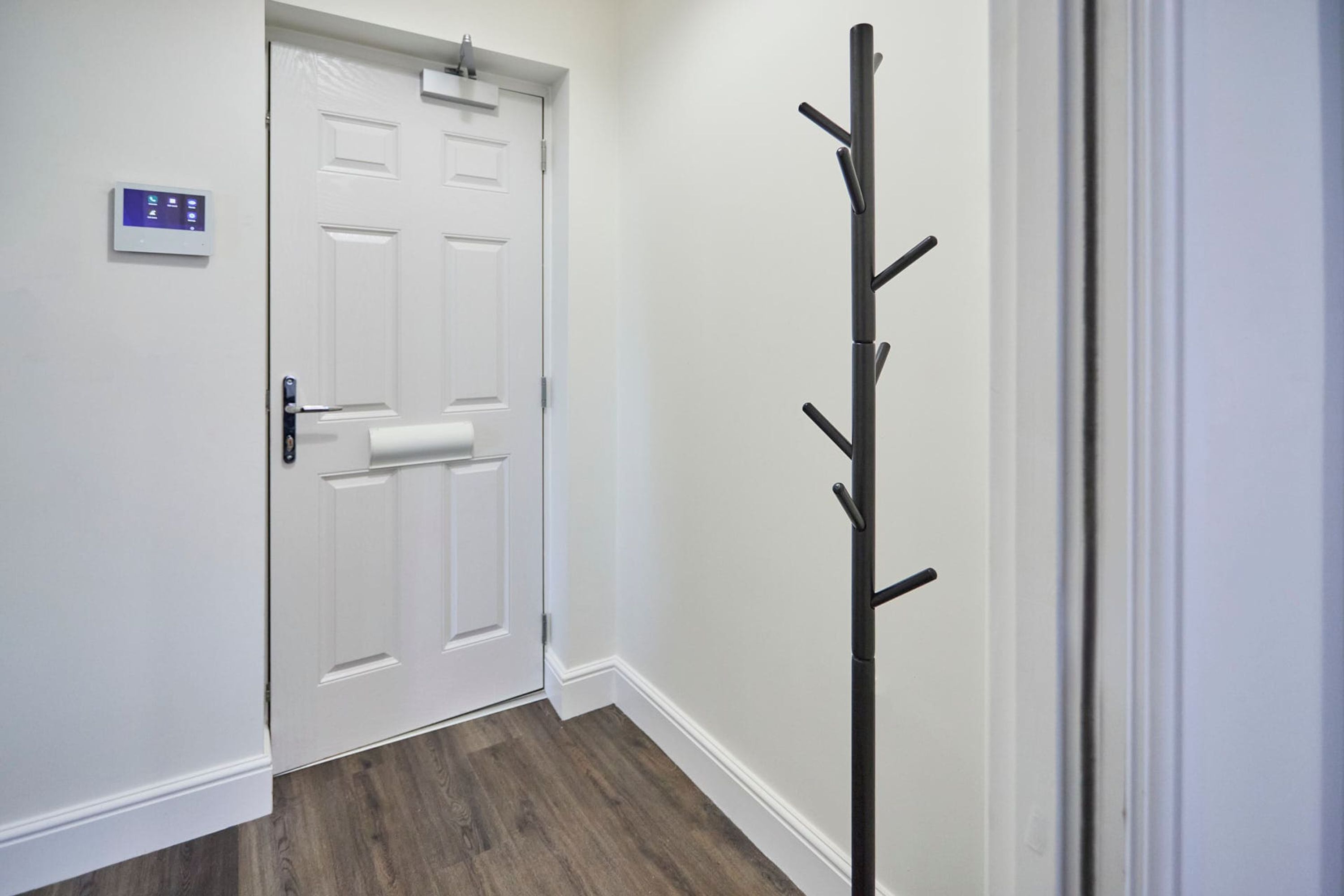 A hallway with a white door, a coat rack, and a thermostat on the wall.