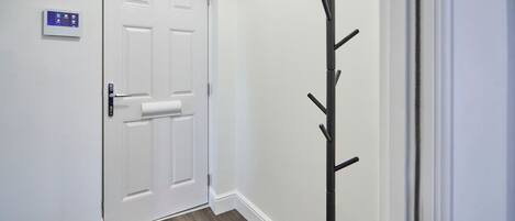 A hallway with a white door, a coat rack, and a thermostat on the wall.