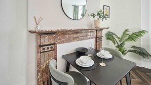 A dining area with a marble fireplace, a round mirror, and a table set with plates, glasses, and a bowl.