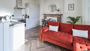 A modern kitchen with white cabinetry, a red velvet sofa, and a dining area with a table and chairs.