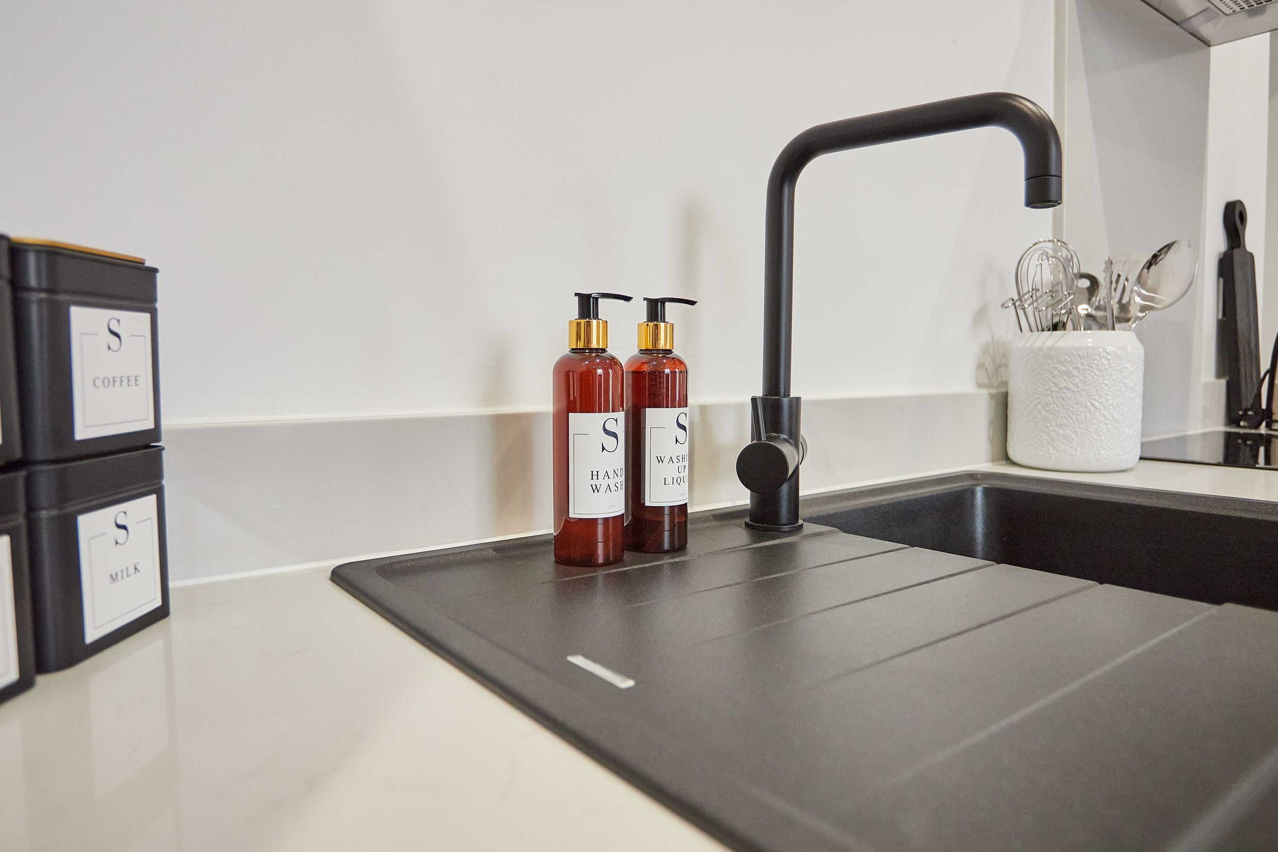 A modern kitchen with a black countertop, a black faucet, and two bottles of hand soap.