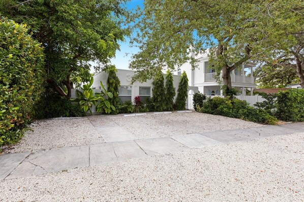 A courtyard with a gravel path, surrounded by lush greenery and a white building with multiple stories and balconies. - Lovely Studio in the Heart of Victoria Park (Fort Lauderdale)