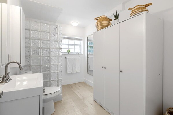 Un baño moderno con cabina de ducha de vidrio, un lavabo blanco y un vestidor amplio.