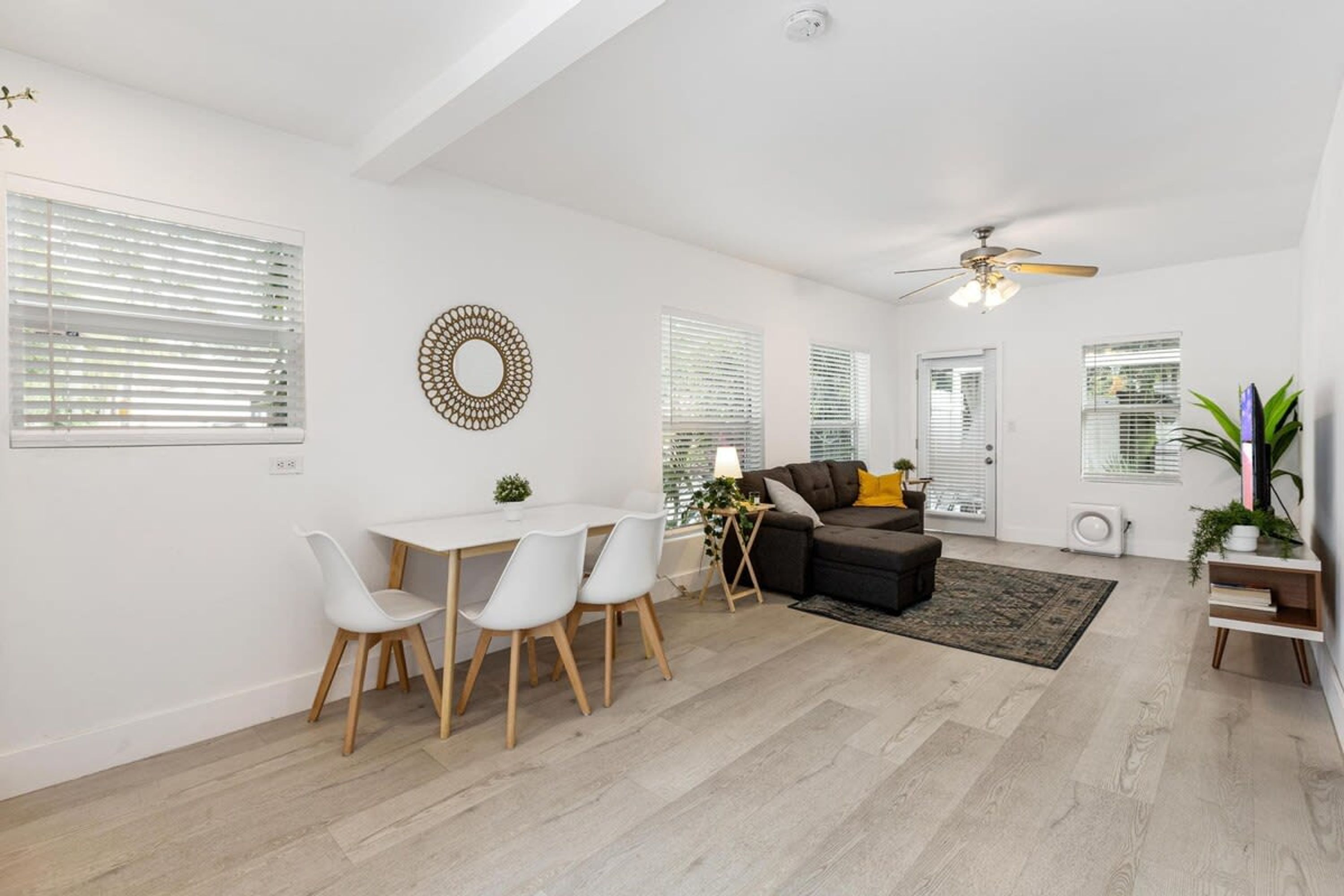 A modern living room with a dining area, white walls, and a ceiling fan.